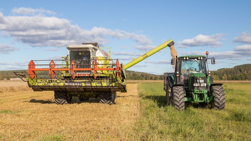CLAAS combine harvester and John Deere tractor during harvest in Swedish farmland